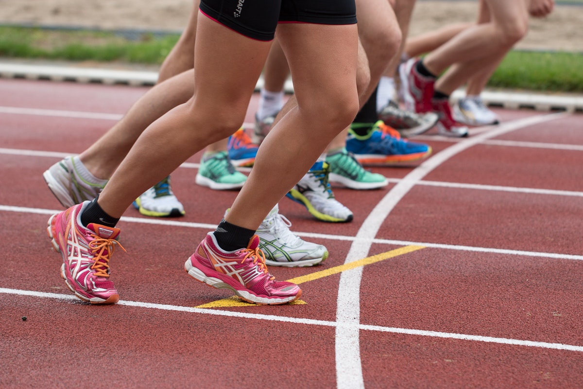 Multiple runners lined up at a starting line. The photo does not show faces, it is a closeup of mulitple runners legs in position to start running.